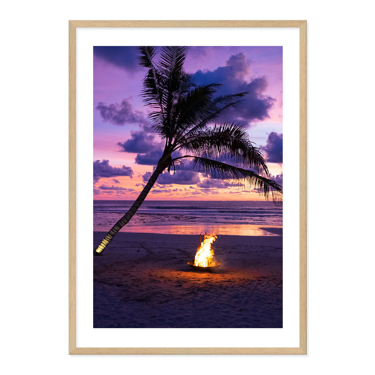 Framed photo of a fire pit by a palm tree on a beach with a sunset sky.
