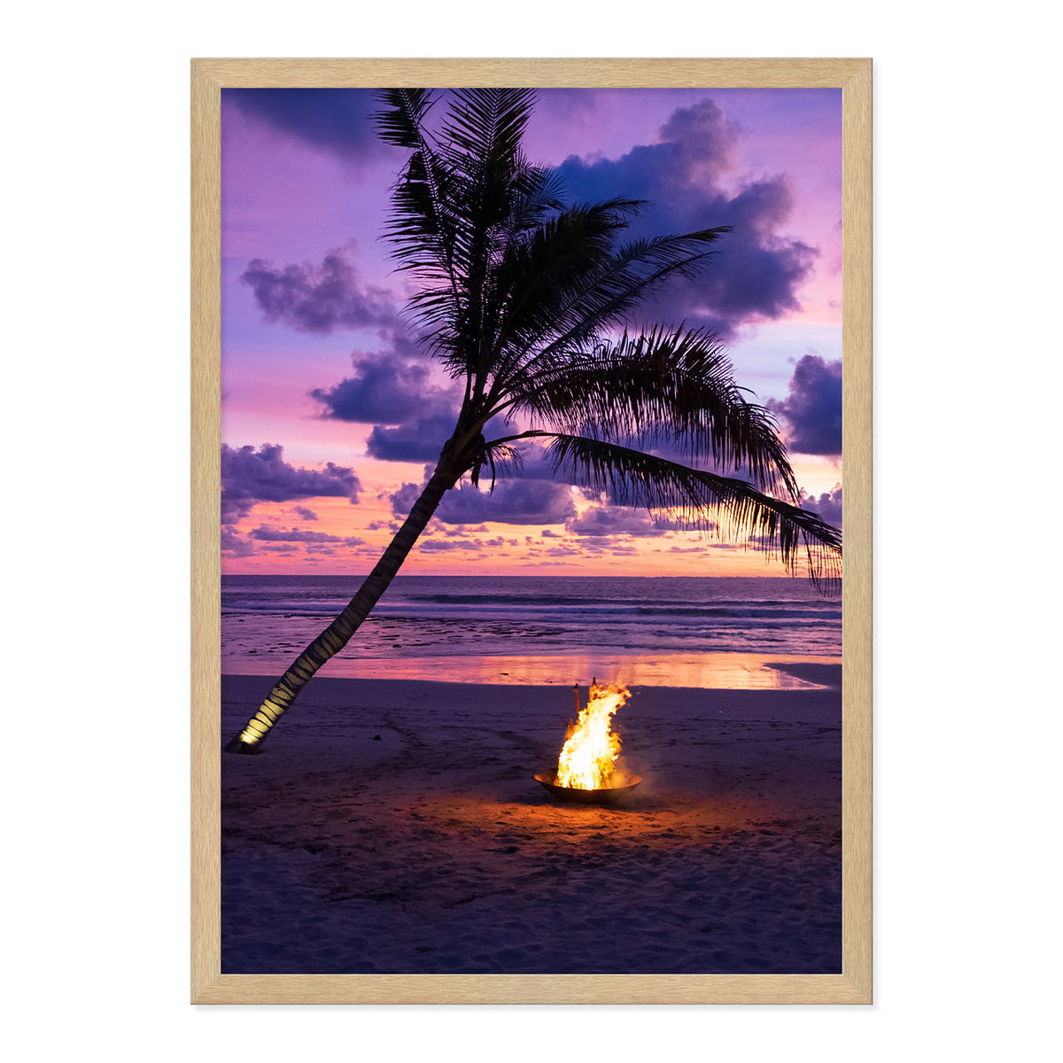Framed photo of a fire pit by a palm tree on a beach with a sunset sky.