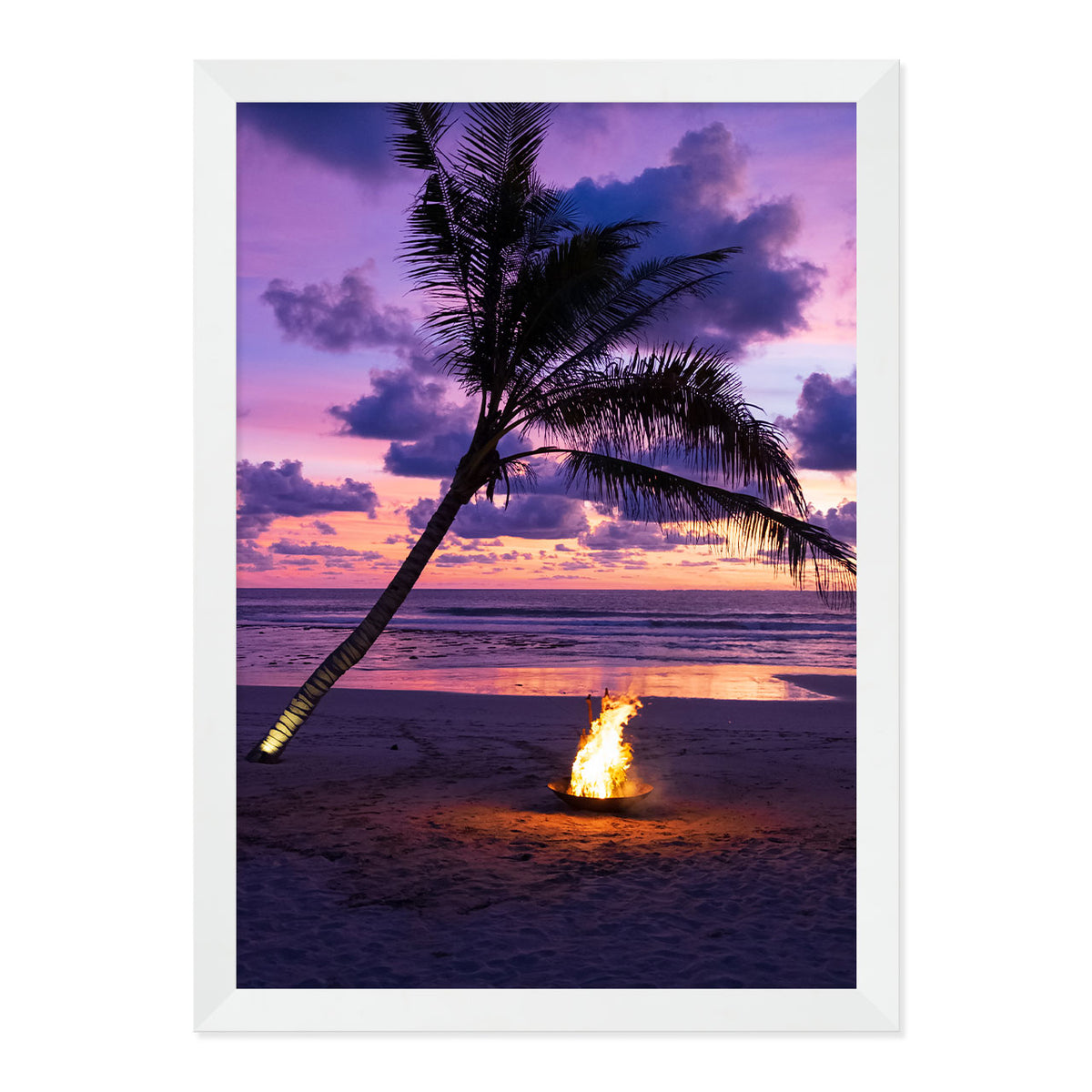 Framed photo of a fire pit by a palm tree on a beach with a sunset sky.