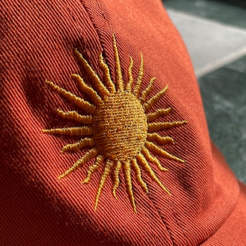 Embroidered yellow sun on a orange fabric cap